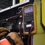 Services Electrician using a multimeter to fix industrial control panel wiring.